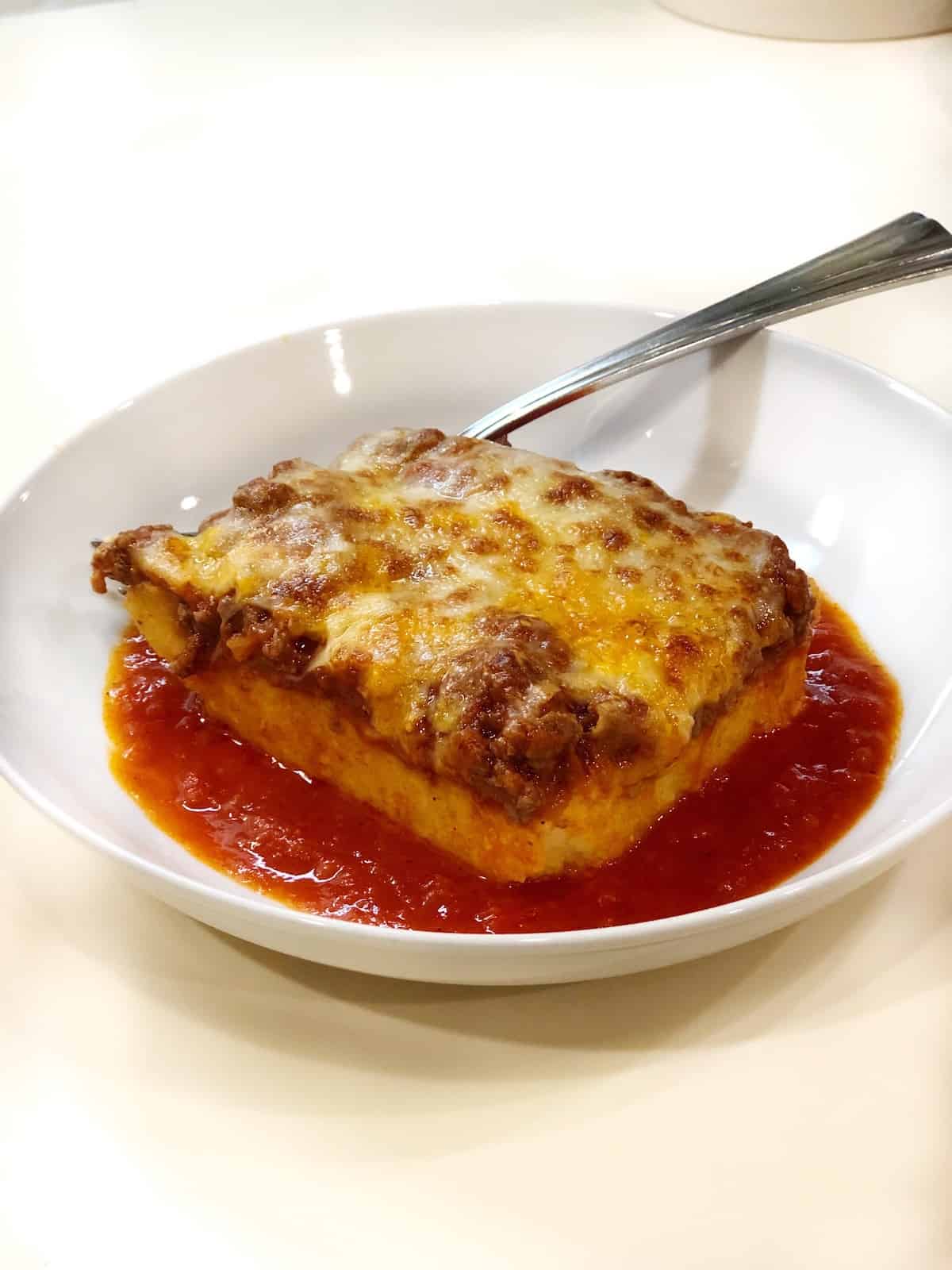 Italian baked polenta with meat sauce in a white bowl with a fork