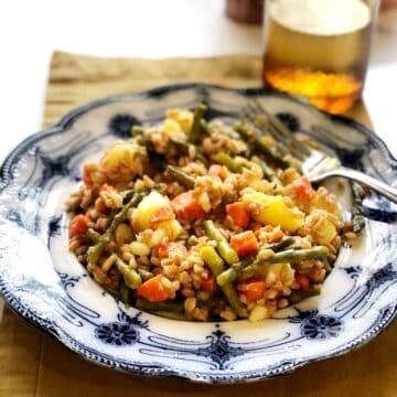 farro salad with vegetables on a plate with a glass of water in background