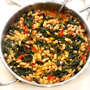 top view of Swiss chard and cannellini beans in a pan on a white counter
