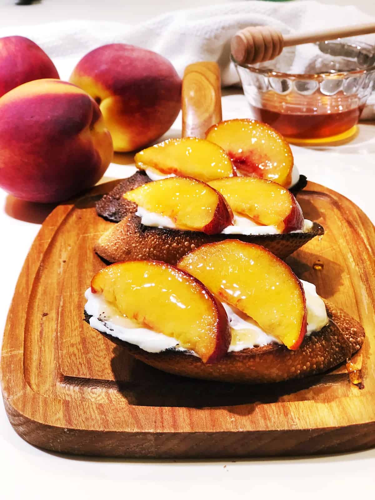 Assembled peach bruschetta on a wood board with peaches in the background.