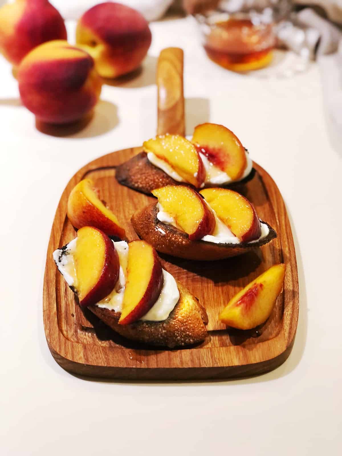 bruschetta with ricotta and sliced peaches on top with honey and peaches in the background.