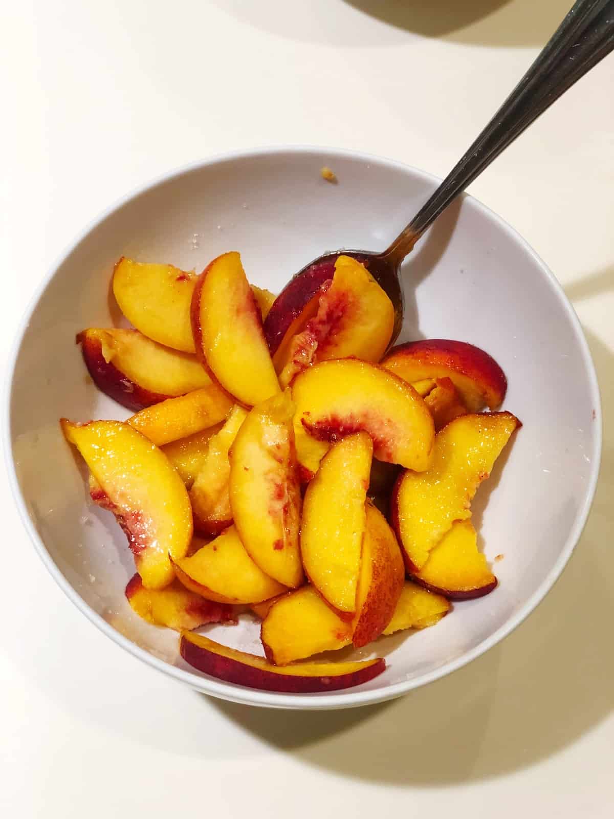 Sliced peaches in a bowl with a spoon.