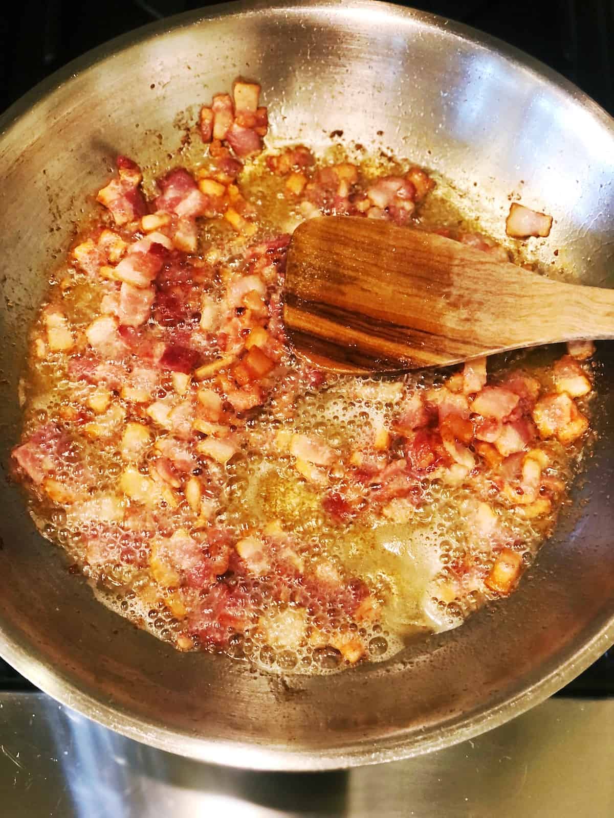 Cooking bacon pieces in a large saute pan.