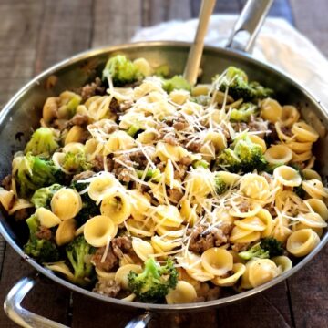 sausage broccolini pasta in a pan on a wood counter with a serving spoon.