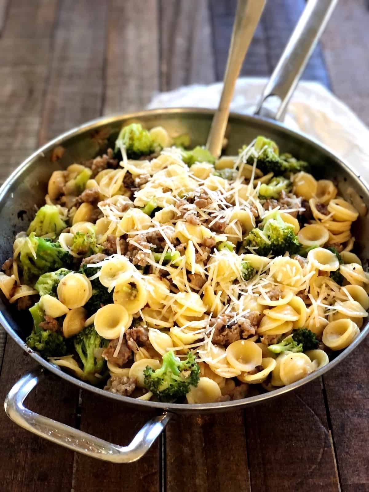 sausage broccolini pasta in a pan on a wood counter with a serving spoon.