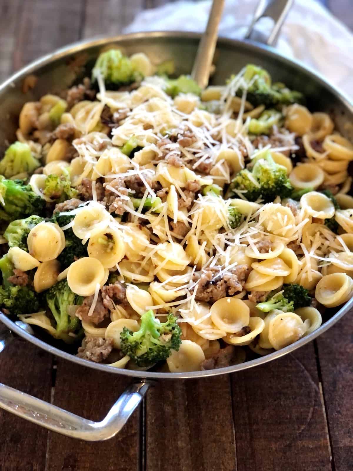 sausage broccolini pasta closeup view in a pan on a wood counter.