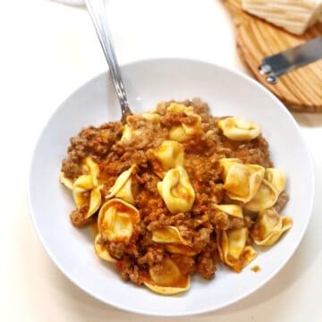 The creamy tortellini Bolognese in a small bowl with Parmesan cheese in background.