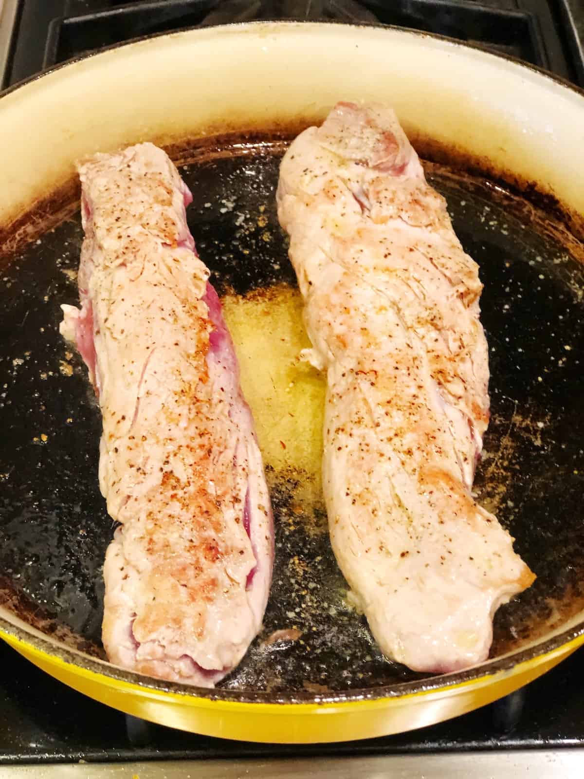 Searing the pork tenderloin in a pan.