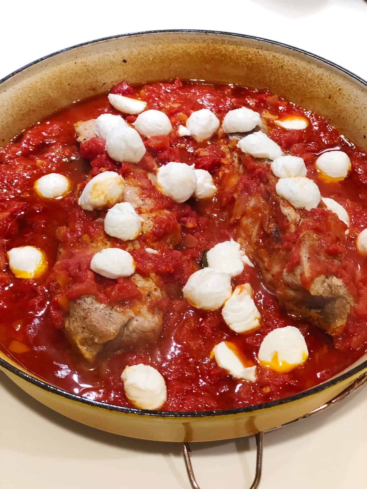 Adding mozzarella to the pork tenderloin in tomato sauce.