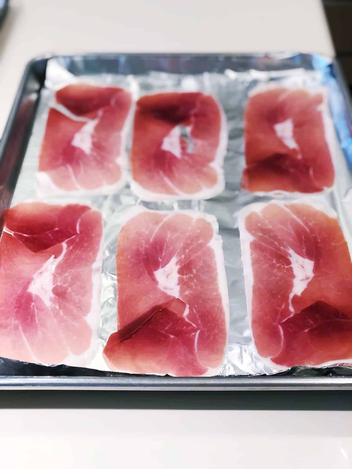 Adding the prosciutto to a sheet pan.