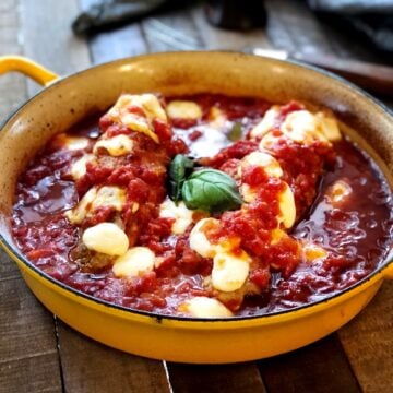 Pork tenderloin in tomato sauce in a large pan on a wood table.