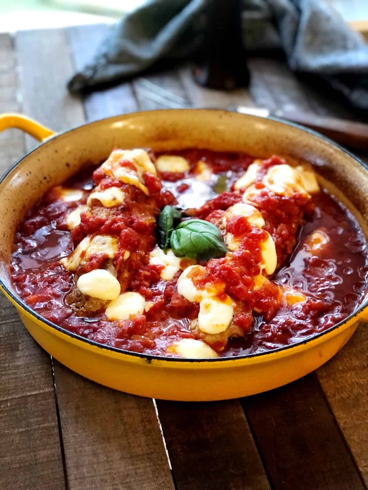 Pork tenderloin in tomato sauce in a large pan on a wood table.