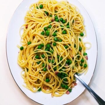 spaghetti alla carbonara with peas and pancetta on an oval plate with a fork.