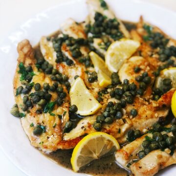 Italian chicken piccata on a plate with lemons over the top.