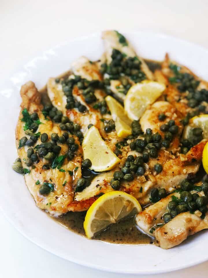 Italian chicken piccata on a plate with lemons over the top.