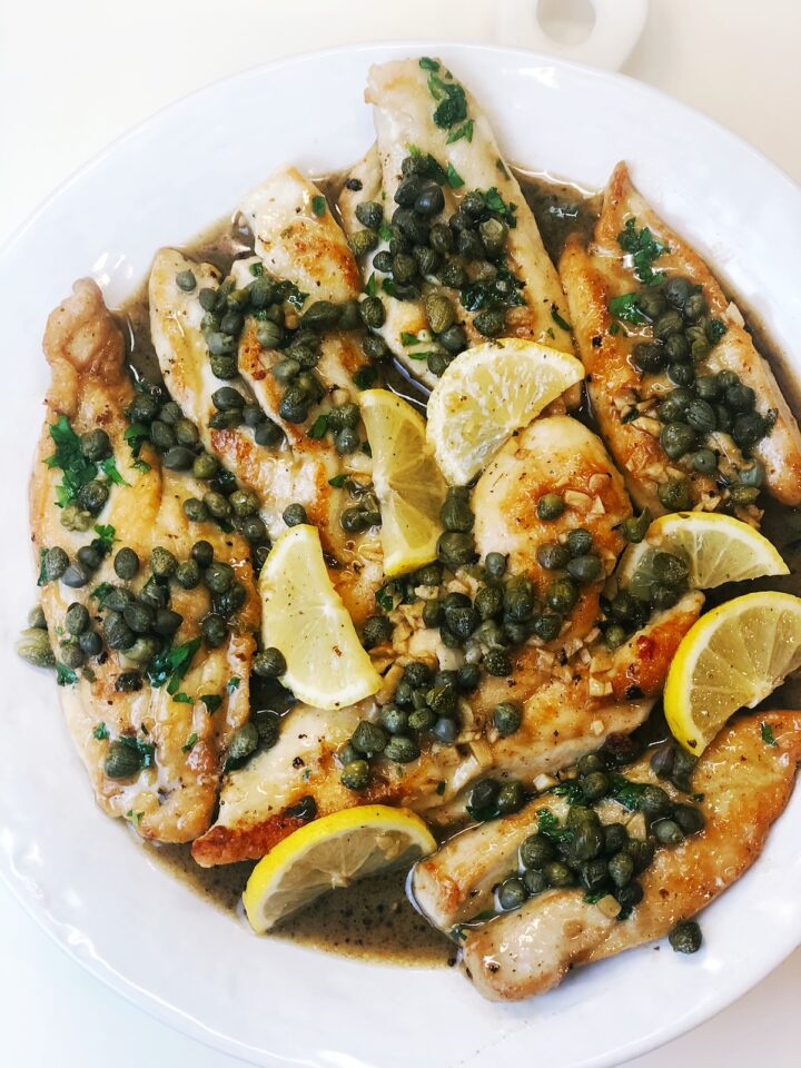 Italian chicken piccata on a plate with lemons over the top and sauce on the plate.