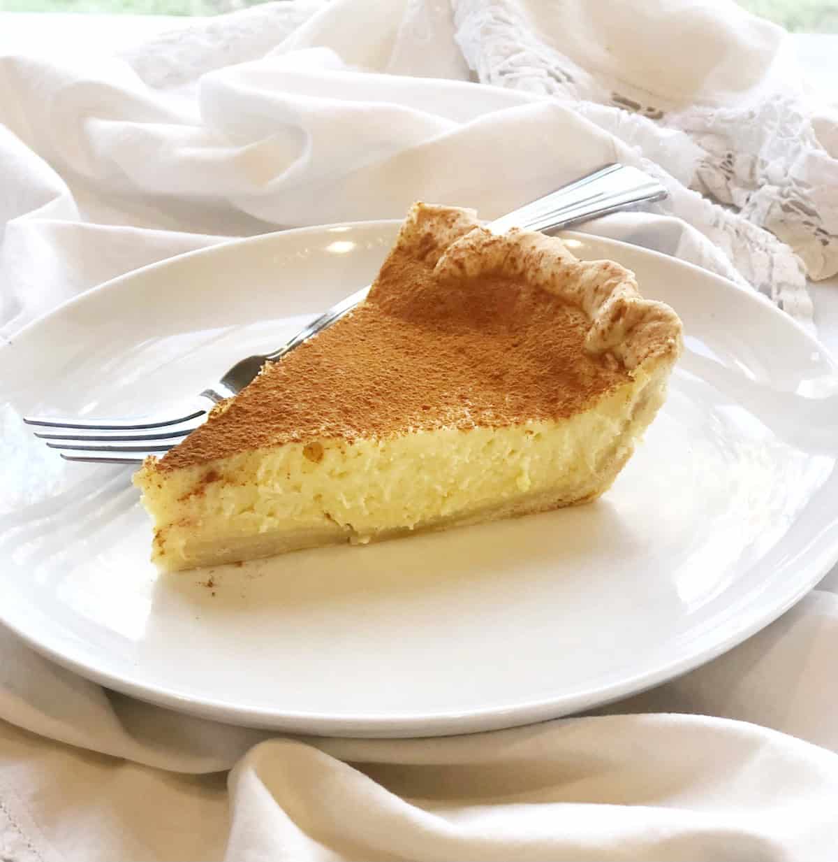 A slice of ricotta pie on a plate with a fork next to it.