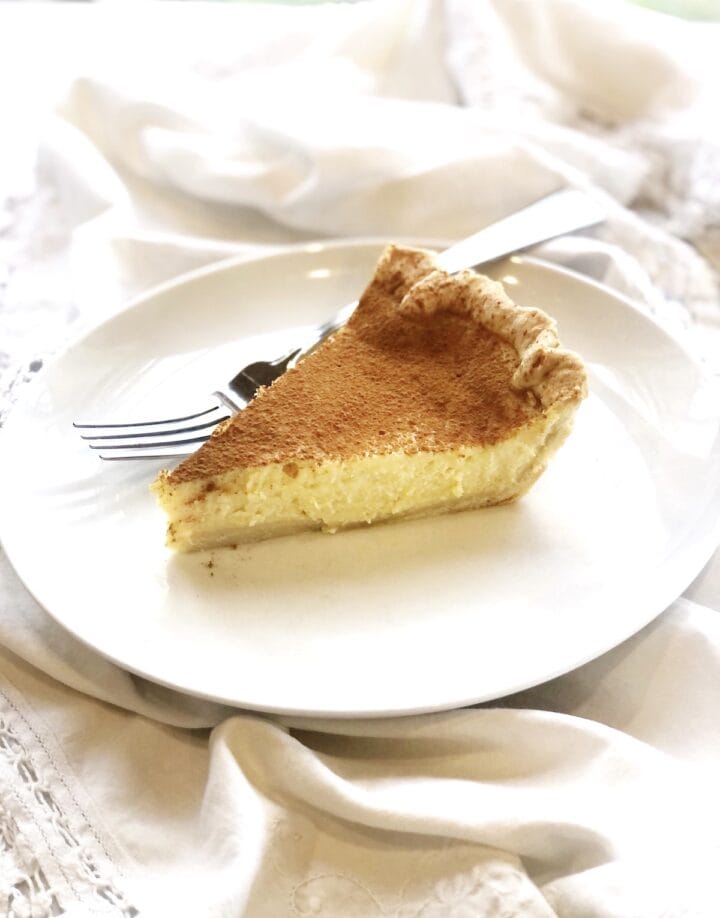 A slice of ricotta pie on a plate with cinnamon on top.