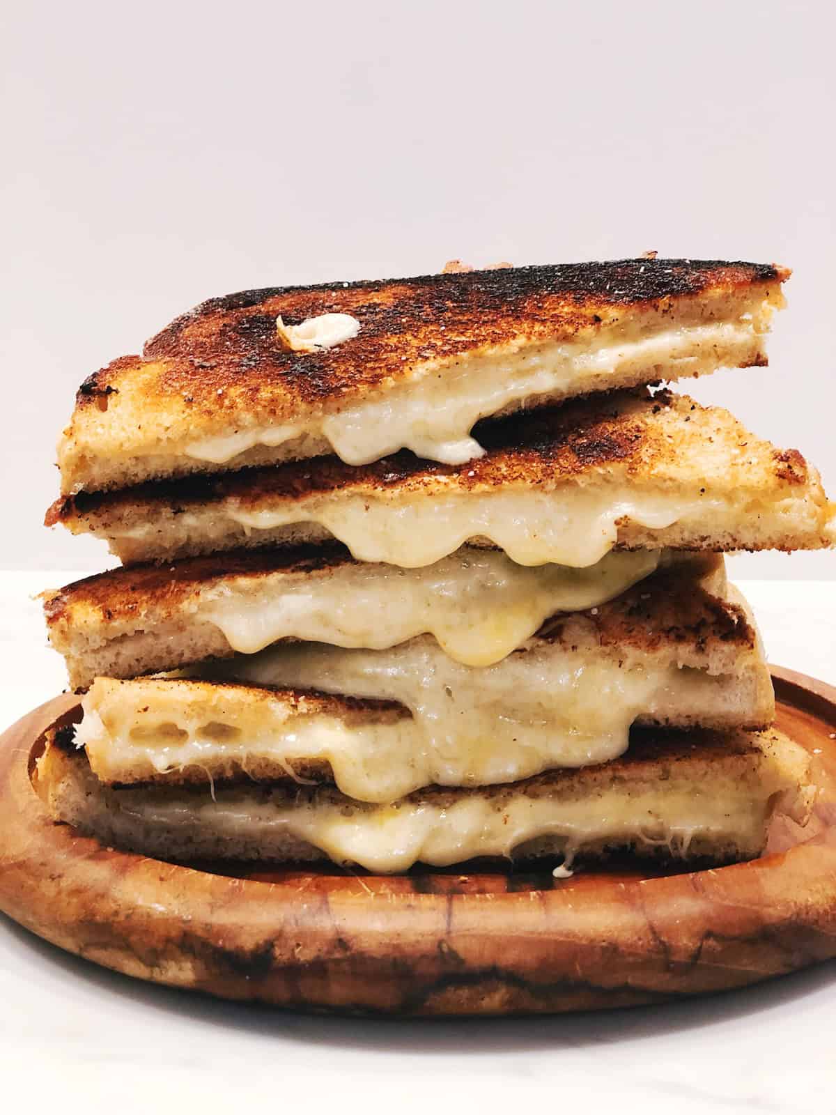 Italian grilled cheese sandwiches sliced in half and stacked up on a wood plate.
