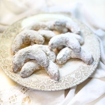 Almond crescent cookies on a plate dusted with powdered sugar.