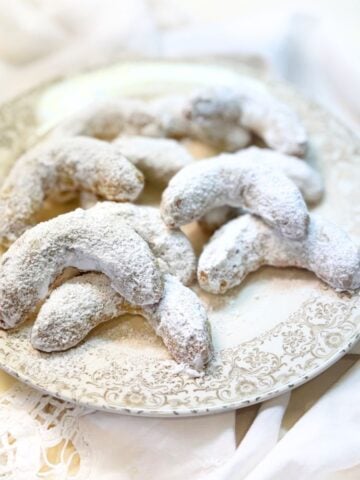 Almond crescent cookies on a plate dusted with powdered sugar.