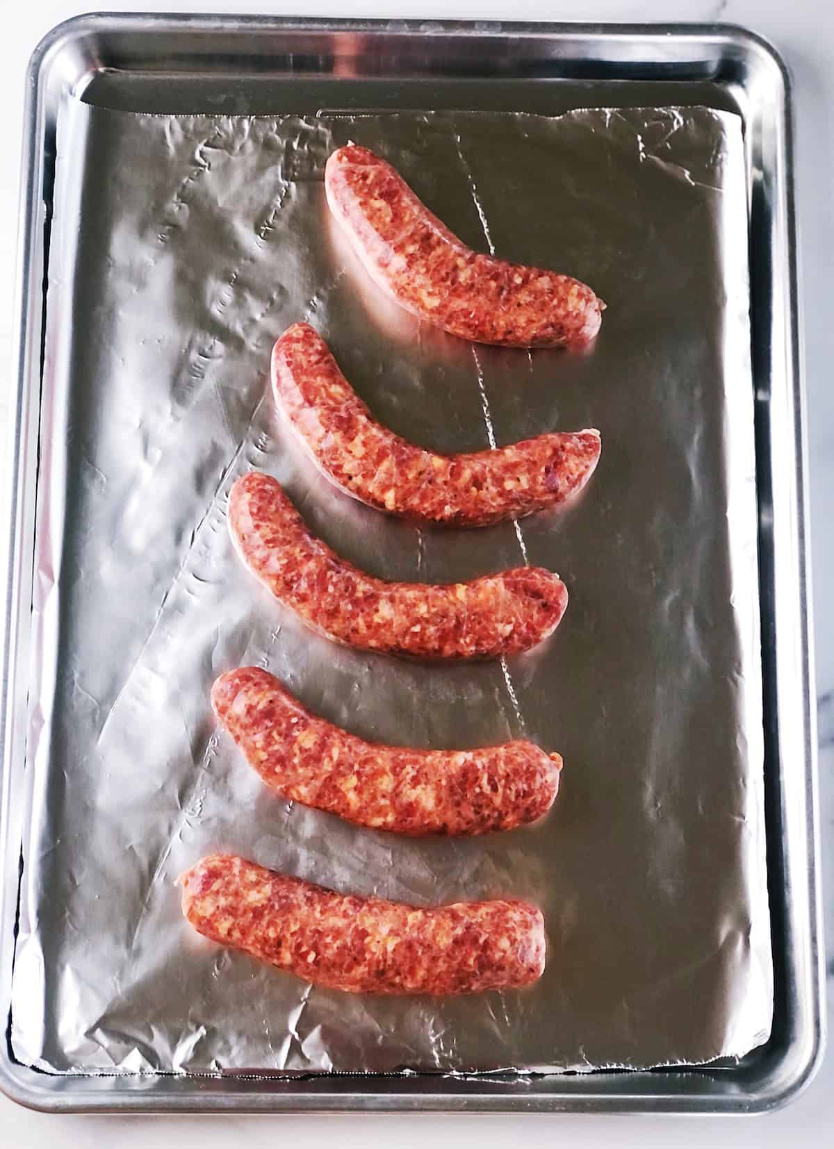 Uncooked Italian sausage on a sheet pan.