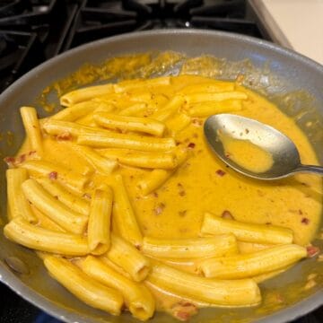 Pumpkin rigatoni in a pan with a spoon.