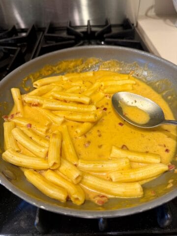 Pumpkin rigatoni in a pan with a spoon.